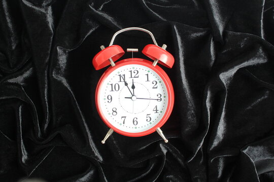 There is a red alarm clock lying on a black velvet fabric.