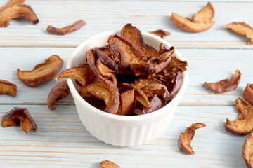 There is a bowl with dried apples on a wooden background.	