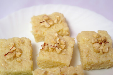 Close-up of soft and creamy Indian kalakand sweet garnished with cashew nut and saffron, served on a white plate. Isolated on white Background.