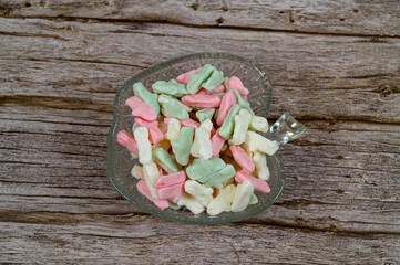 Brightly colored candy pieces in pastel shades are arranged in a crystal dish on a weathered wooden table. They create a cheerful and inviting display ideal for snacking or sharing