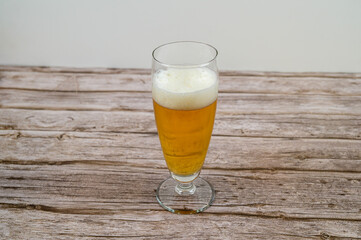 Golden beer fills a tall glass with a frothy head, resting on a weathered wooden table with a simple background. The drink invites relaxation and enjoyment