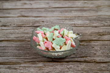 Brightly colored candy pieces in pastel shades are arranged in a crystal dish on a weathered wooden table. They create a cheerful and inviting display ideal for snacking or sharing