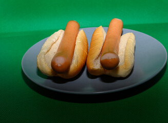 Two hot dogs placed in soft buns sit on a round gray plate. The vibrant green background adds a lively touch, perfect for a casual meal or gathering at home
