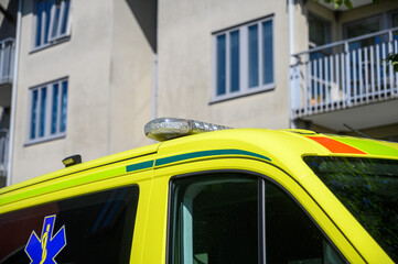 An emergency medical vehicle is parked near a residential building. The bright yellow design of the vehicle stands out against the backdrop of the modern architecture