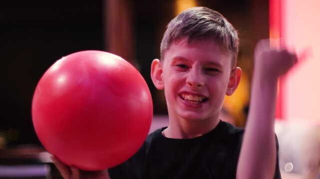 portrait of cheerful handsome Caucasian boy 10-11 years old holding bowling ball in hands and rejoicing in victory, child in bowling club having fun