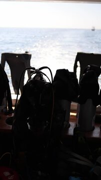 Vertical screen scuba diving gear with tanks wetsuits and BCDs ready on deck bright ocean sparkles in background scene captures thrill of exploration and underwater adventure