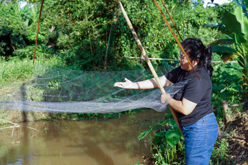 Asian woman tries out a fishing net, a traditional Thai tool used to catch fish in a stream.