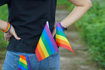Asian LGBT woman wearing a black T-shirt and a rainbow wristband stands with her hands on her hips, holding a rainbow flag, a symbol of LGBT pride, in her back pocket.
