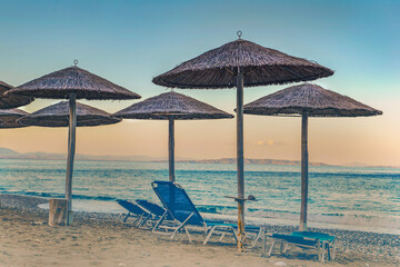 straw umbrella and sun loungers on a beach at sunset in Peloponnese Greece
