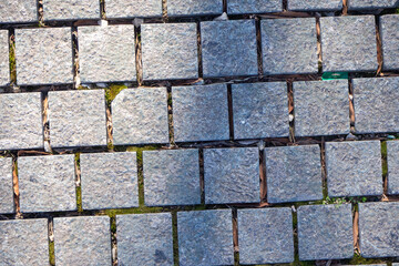 Natural stone paving with green moss in joints. Illustrates eco-friendly urban landscaping. Diagonal arrangement. Architectural background.