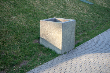 Square Concrete Trash Can on Gras. Concrete outdoor trash can with square shape placed on grass near a stone path. Designed for public park waste disposal. Urban landscape element.