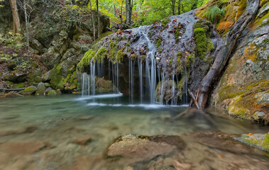 Fototapeta premium Russia, Republic of Crimea. View of the waterfall on the Ulu-Uzen River in the shade of the rocky thickets of the mountain gorge of the Haphal Hydrological Reserve.
