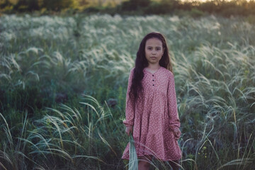 A girl with long dark hair stands in a field