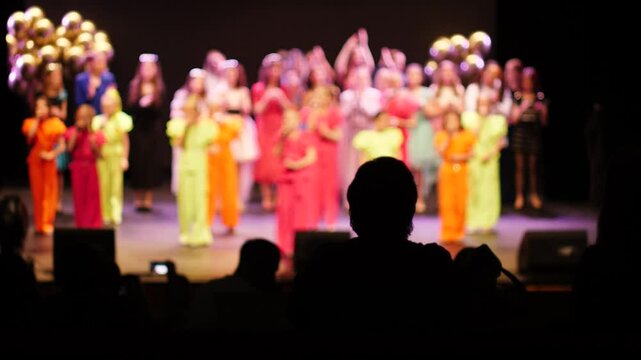 children's concert on stage out of focus, in the auditorium the audience clap their hands and dance, children's reporting concert for parents