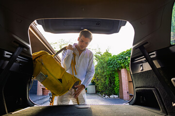 Young tourist putting his backpack in car trunk preparing for road trip