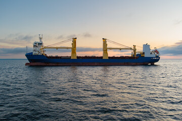 A freighter with a blue hull and bright yellow cranes in the Baltic during sunset. Aerial shot from...