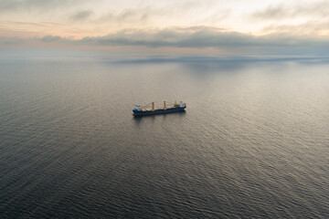 Fototapeta premium Impressive aerial panorama: General cargo ship in the Baltic Sea at sunset, drone shot. Calm sea, soft cloudy sky.