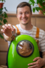 Smiling man holding keys to his new property, carrying his cat in a pet carrier backpack, excited...