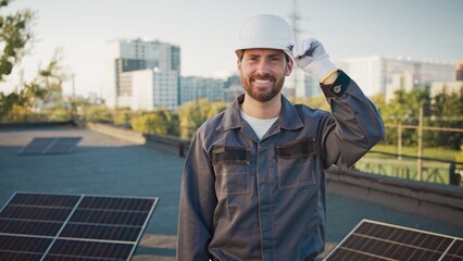 Caucasian male standing on rooftop wearing work uniform and helmet, crossing arms confidently....