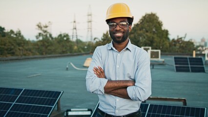 African American man engineer in reflective vest and yellow hard hat stands confidently on a rooftop near solar panels. Male worker symbolizing commitment to sustainable energy and innovation.
