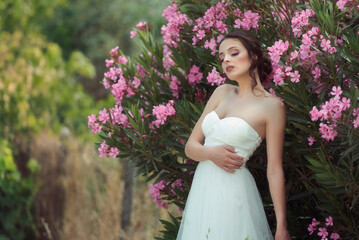 Dreamy woman in white dress leaning on blooming oleander bush