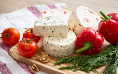 Variety of home made cheese and paprica and herbs, olive oil, olives and bread on a wooden board. Brined curd white cheese with vegetables on the table