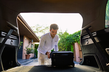 Young businessman putting suitcase in car trunk before trip