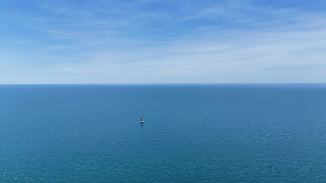 Lone Sailboat Floating in Vast Open Sea Under Serene Blue Sky