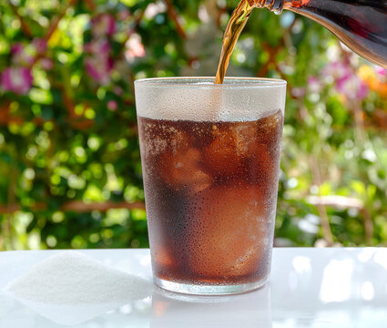 Refreshing, sugary cola drink, served with ice outdoors with a garden background.