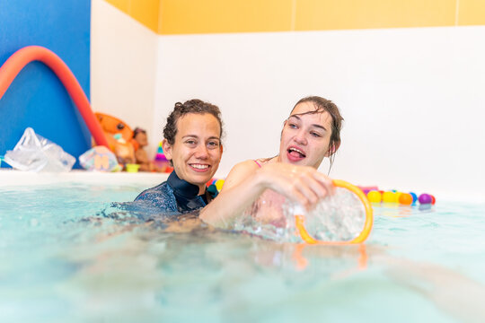 Young woman with cerebral palsy exercises with physiotherapist in a hydrotherapy pool - Empowerment and movement training in water. Concept of cerebral palsy, hydrotherapy, physiotherapist



