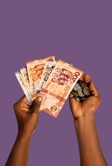 Black African hands in holding Ghanaian cedi notes and coins on purple background

