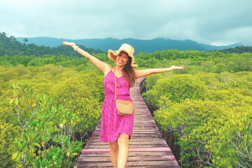 Beautiful asian woman smiling brightly stading on wooden bridge among mangrove forest, happy woman concept