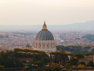 Aerial sunset view of Vatican dome dominating central Rome, with Renaissance detail, glowing sky and scenic landscape in soft golden tones.