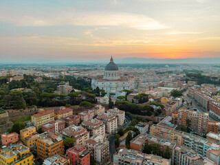 Peaceful cityscape of Rome at dusk, dominated by St. Peter’s Basilica’s towering dome, glowing against the warm and fading sunset sky. Travel concept