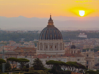 Aerial sunrise view of Vatican dome dominating central Rome, with Renaissance detail, glowing sky and scenic landscape in soft golden tones.