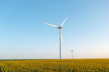 Silhouettes windmills, large orange sun disc summer lens flare. Alternative energy wind turbines with blades in field aerial view bright orange sunset blue sky wind park slow motion drone turn