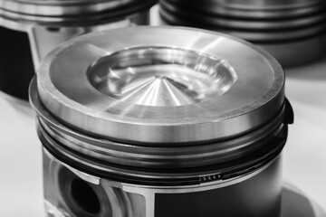 A close up of a piston with a cone shaped top. The piston is silver and has a black rim auto...