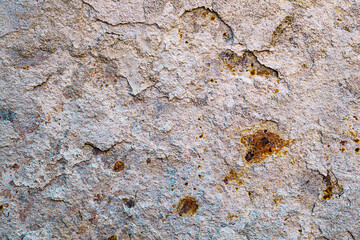 Background of a light beige metal wall from which layers of hardened cement mortar are peeling off, and the exposed areas are covered with brown, deep rust. Properties of structural materials