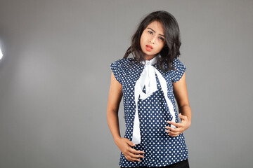 A confident, stylish young woman, wearing a polka-dot blouse and black trousers, posing against a...