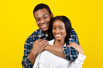 Naklejka premium Love, date, relationship, family and happy together. Smiling millennial african american man hugging wife in casual and look at camera, isolated on yellow background, studio shot, free space