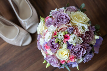 Bridal bouquet of pastel roses with wedding shoes. A top-down view of an elegant pastel bridal bouquet featuring roses in shades of lavender, white, pink.