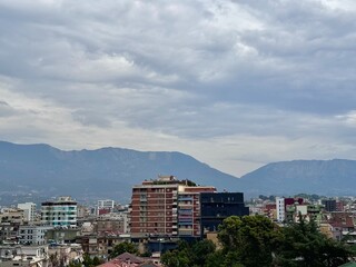 view of buildings in the city of Tirana with mountains in the background on a cloudy summer day
