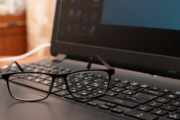 Fototapeta premium Glasses resting on a black laptop keyboard in the home office during daylight hours while not in use