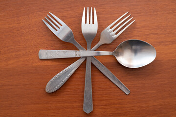 Arrangement of three forks and one spoon intersecting at their centers on a wooden table