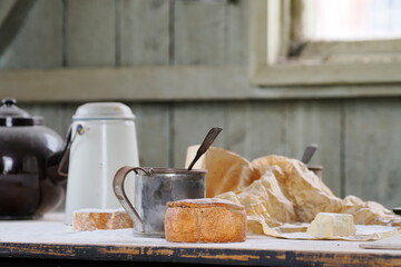 Rustic kitchen scene with bread, cheese and metal mugs, and vintage cookware on a flour-dusted table.