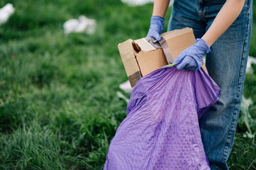 Volunteer picking up trash in park putting cardboard box in garbage bag