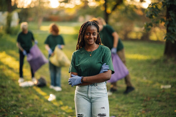 Young black woman volunteer crossing arms while picking up trash in park