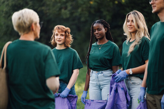 Group of volunteers picking up trash in park listening to instructions - Powered by Adobe