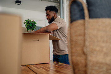Man unpacking cardboard box with plant in new home