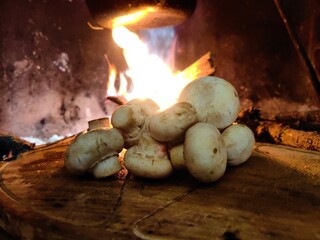 Mushrooms on the wooden kitchen board in front of fireplace and fire flame background
